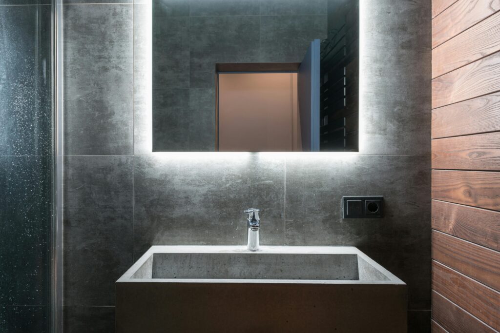 Sleek modern bathroom featuring an illuminated mirror, concrete sink, and elegant gray tiles.